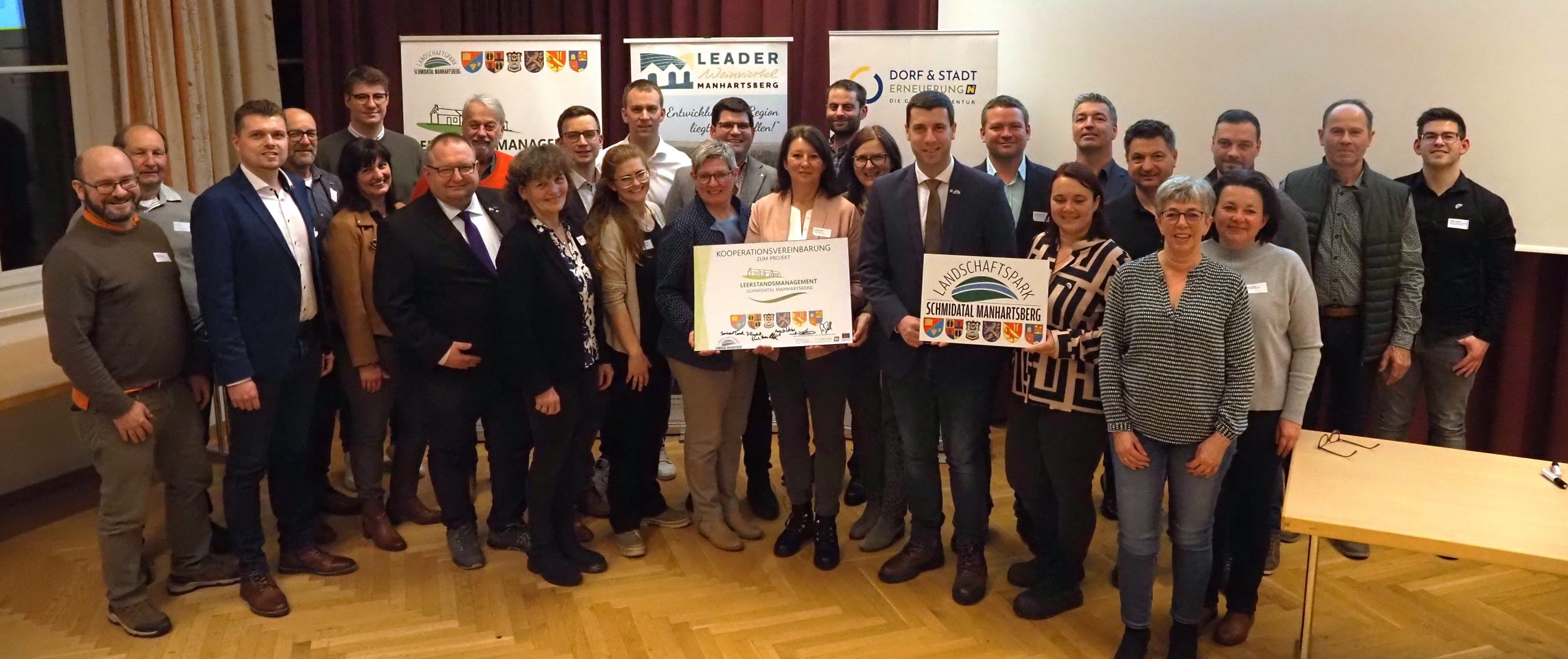 Pressefoto_KickOff Gruppe von Menschen die in einem Veranstaltungssaal gesammelt auf die Bühne getreten sind um Einigkeit zum Willen in der Bearbeitung des Thema Leerstandes zu signalisieren.